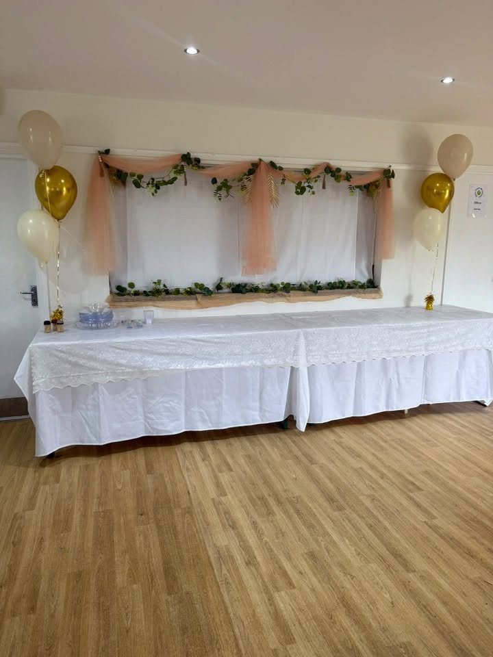 A buffet table dressed with white cloths, drapes, greenery and balloons