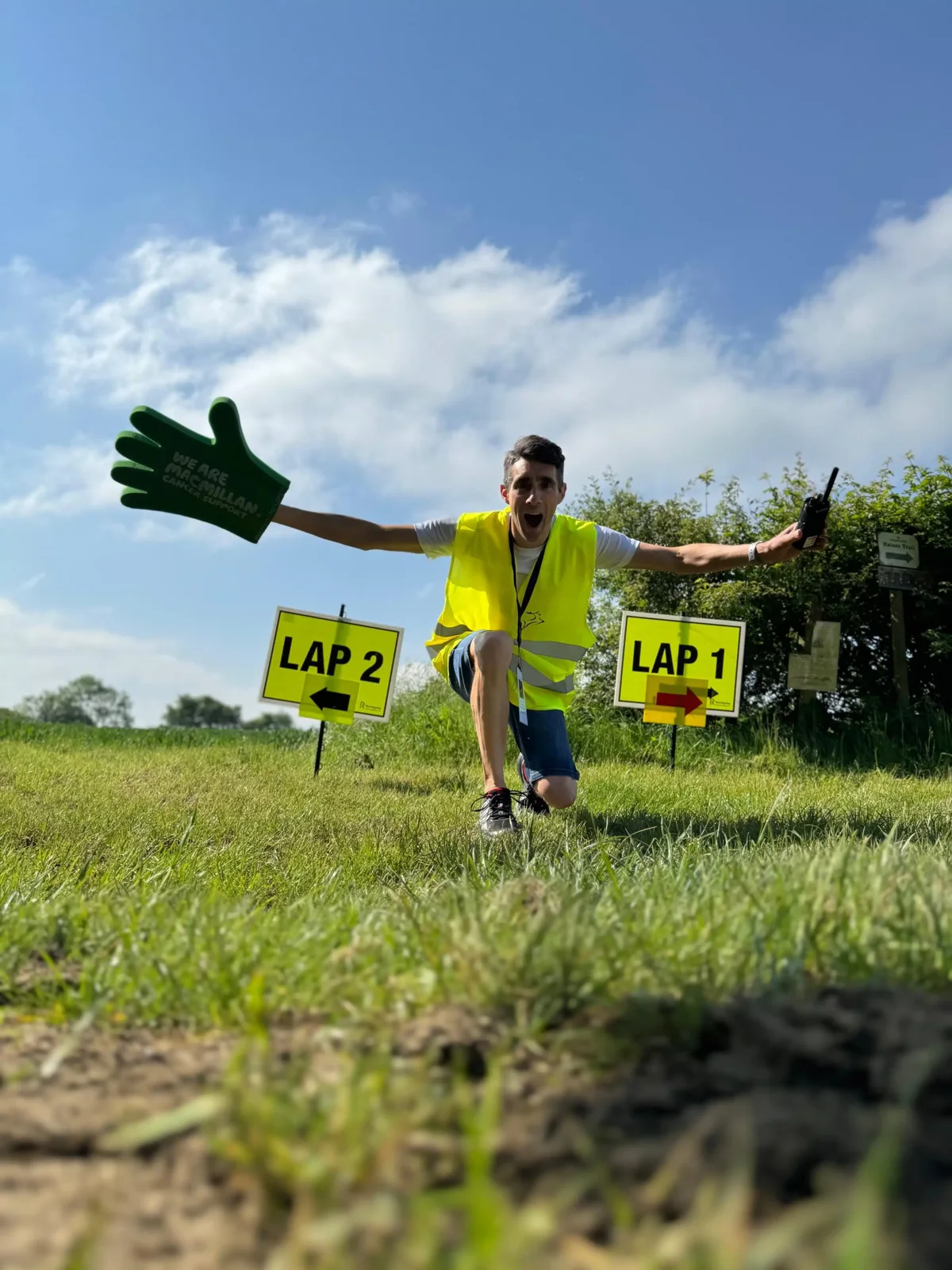 A Stort10 marshal in hi-vis and a giant foam hand cheering runners on by the lap signs